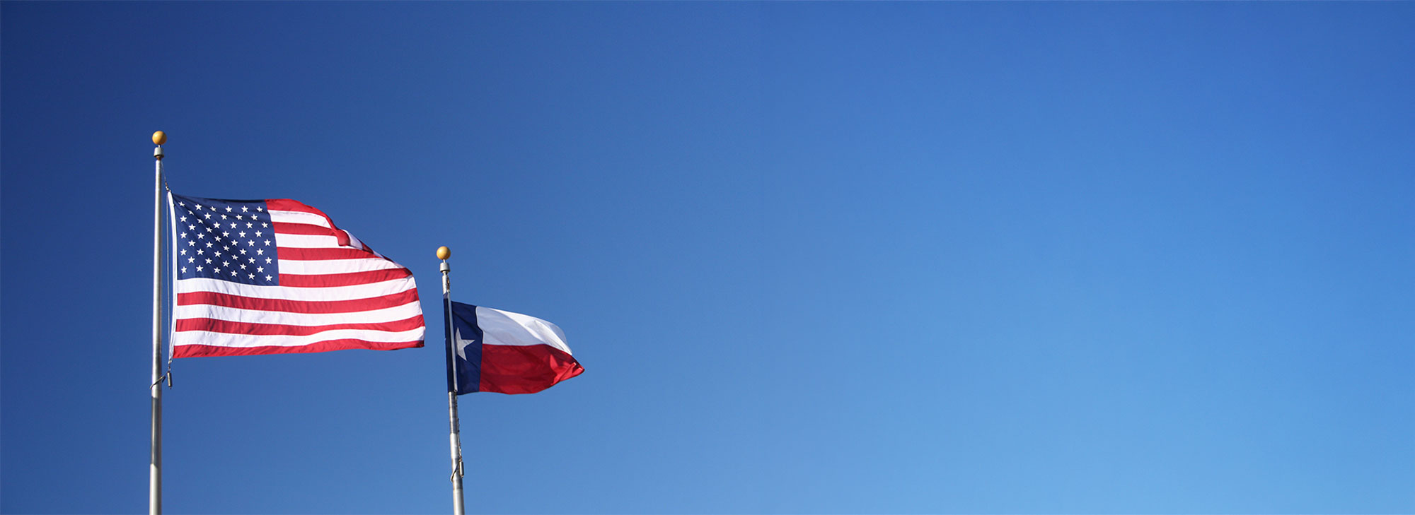 A US flag and Texas state flag flying beside each other
